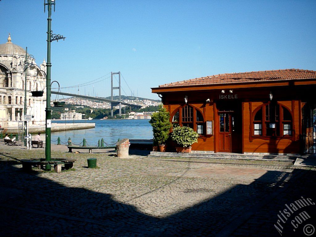 View of the jetty, Bosphorus Bridge, Ortakoy Mosque and the moon seen in daytime over the bridge`s legs from Ortakoy shore in Istanbul city of Turkey.
